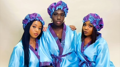 Three women wear IMROK's blue and purple robes and bonnets.